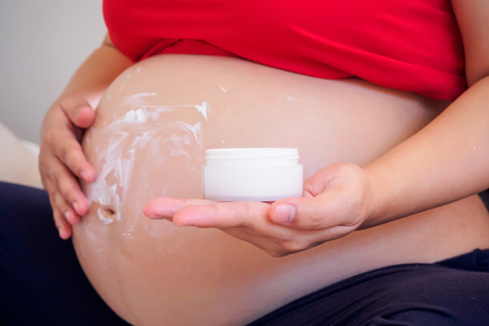 Pregnant Woman applying stretch marks cream on her bellyの写真素材