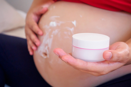 Pregnant Woman applying stretch marks cream on her bellyの写真素材