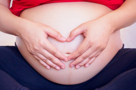 Asian pregnant woman Hands forming heart on her bellyの写真素材