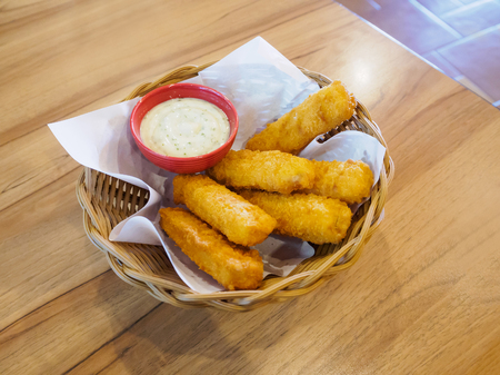 fresh fish fingers sticks with sauce in basket on wood tableの写真素材