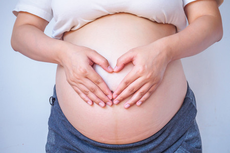 pregnant woman hands forming heart on her bellyの写真素材