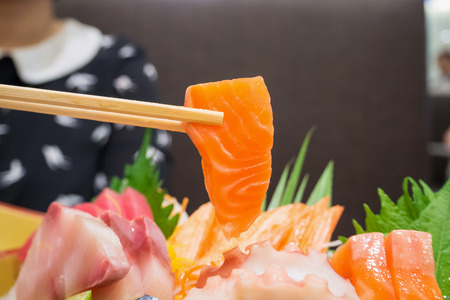 salmon in chopsticks with japanese sashimi set on boat plateの写真素材