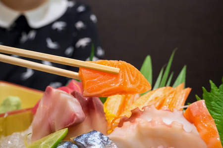 salmon in chopsticks with japanese sashimi set on boat plateの写真素材
