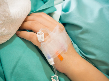 Asian woman patient hand on IV drip with saline solution, fluid replacement therapyの写真素材
