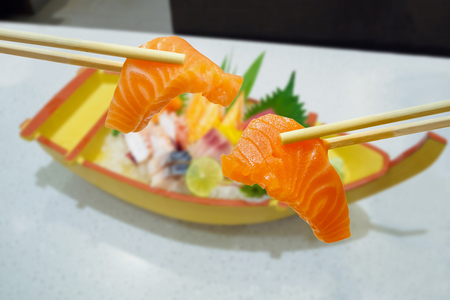 salmon in chopsticks with japanese sashimi set on boat plateの写真素材