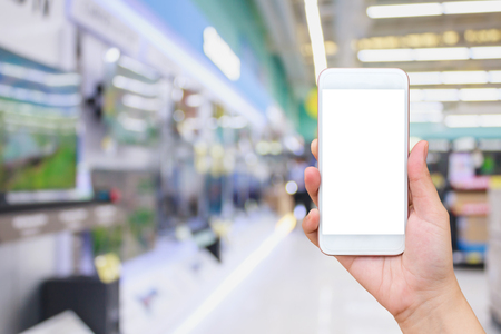Hand hold mobile smartphone with Television show in electronic department store in shopping mall with bokeh light defocused blurred background, online shopping conceptの写真素材
