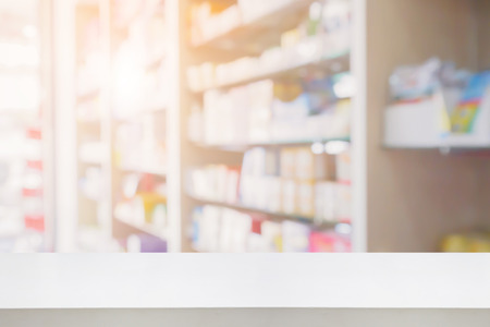 blank white wood table counter in pharmacy store interior with medicine, vitamin, food supplement and healthcare product on medical shelves blur drugstore for background, for create product display templateの写真素材