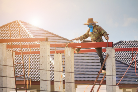Construction welder workers installing steel frame structure of the house roof at building construction site with clouds and skyの写真素材