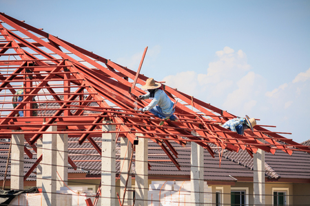 Construction welder workers installing steel frame structure of the house roof at building construction site with clouds and skyの写真素材