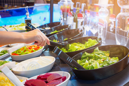 Asian woman choosing vegetable ingredients at salad bar buffet restaurantの写真素材
