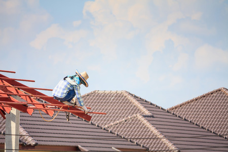 Construction welder workers installing steel frame structure of the house roof at building construction site with clouds and skyの写真素材