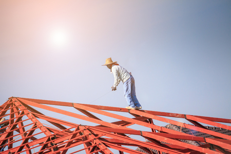 Construction welder workers installing steel frame structure of the house roof at building construction site with clouds and skyの写真素材