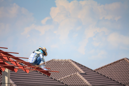 Construction welder workers installing steel frame structure of the house roof at building construction site with clouds and skyの写真素材