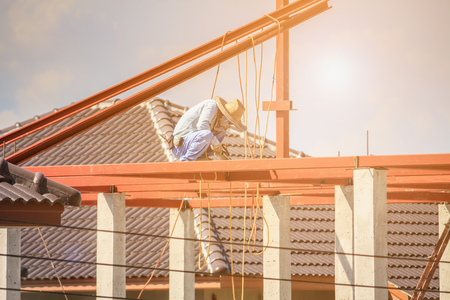 Construction welder workers installing steel frame structure of the house roof at building construction site with clouds and skyの写真素材