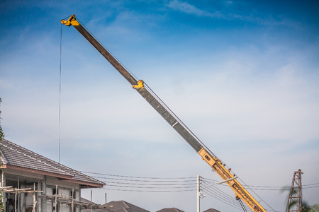 yellow telescopic arms of mobile construction crane truck lifting concrete slab to building house at construction siteの写真素材