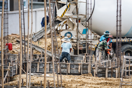 Concrete pouring from cement mixers truck while construction worker laying concrete to the floors beams of buildingの写真素材