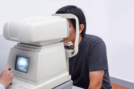 Young handsome asian man take eye exam with optical eye test machineの写真素材
