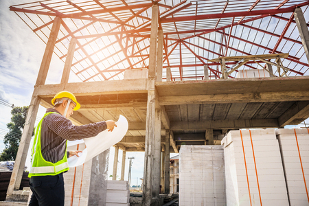 Asian business man construction engineer worker in protective helmet and blueprints paper on hand at house building siteの写真素材