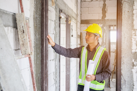 Asian business man construction engineer worker in protective helmet and blueprints paper on hand at house building siteの写真素材