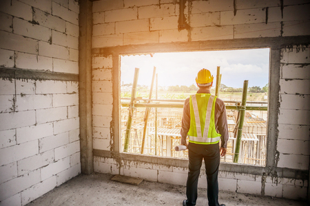 Asian business man construction engineer worker in protective helmet and blueprints paper on hand at house building siteの写真素材