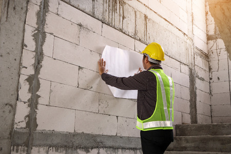 young professional engineer worker in protective helmet working at house building construction site with blueprintの写真素材