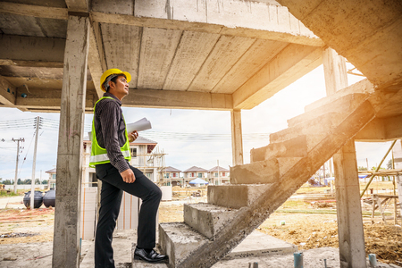 young professional engineer worker in protective helmet and blueprints paper on hand at the house building construction siteの写真素材