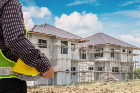 Asian business man construction engineer worker in protective helmet and blueprints paper on hand at house building siteの写真素材