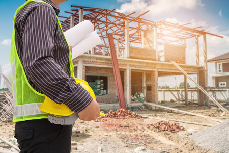 Asian business man construction engineer worker in protective helmet and blueprints paper on hand at house building siteの写真素材