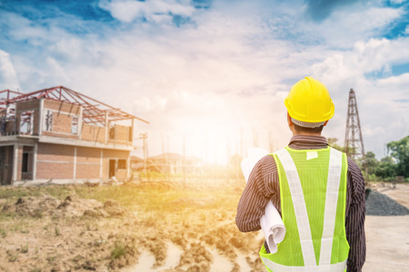 Asian business man construction engineer worker in protective helmet and blueprints paper on hand at house building siteの写真素材