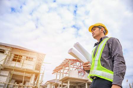 Asian business man construction engineer worker in protective helmet and blueprints paper on hand at house building siteの写真素材