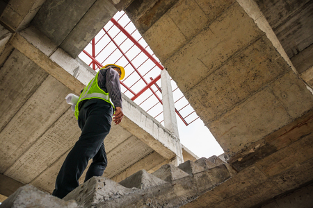 young professional engineer worker in protective helmet and blueprints paper on hand at the house building construction siteの写真素材