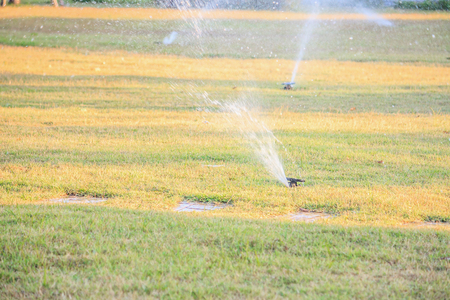 Automatic lawn sprinklers watering over green grass in the gardenの写真素材