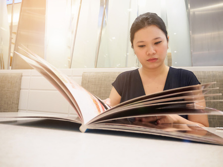 Beautiful young asian woman looking and reading food menu in luxury cafe restaurantの写真素材