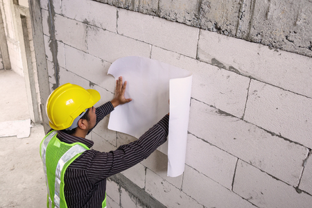 young professional engineer worker in protective helmet working at house building construction site with blueprintの写真素材
