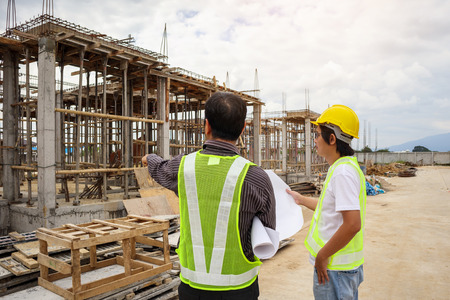 Asian business man construction manager and engineer worker in protective helmet hold blueprints paper on hand at house building siteの写真素材