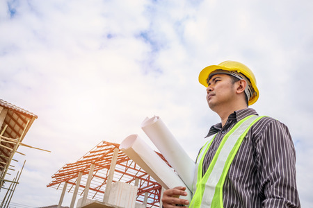 Asian business man construction engineer worker in protective helmet and blueprints paper on hand at house building siteの写真素材