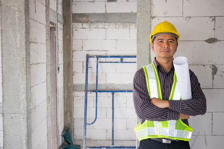 Asian business man construction engineer worker in protective helmet and blueprints paper on hand at house building siteの写真素材