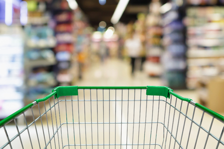 blur supermarket aisle with empty green shopping cart backgroundの写真素材