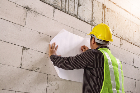 young professional engineer worker in protective helmet working at house building construction site with blueprintの写真素材
