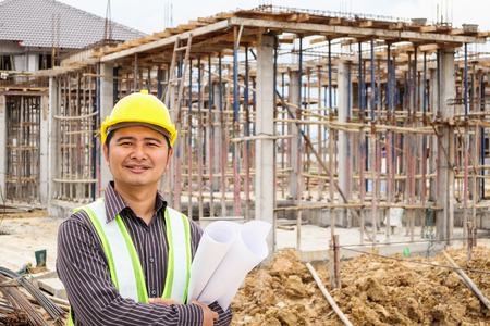 Asian business man construction engineer worker in protective helmet and blueprints paper on hand at house building siteの写真素材