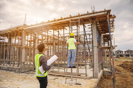 Asian business man construction manager and engineer worker in protective helmet hold blueprints paper on hand at building siteの写真素材
