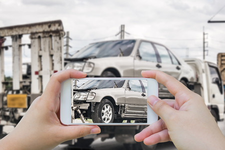 Hand using smartphone photograph the Broken car on tow truck after traffic accident for car insuranceの写真素材
