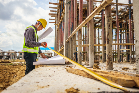 Asian business man construction engineer worker in protective helmet and blueprints paper on hand measuring concrete floor at house building siteの写真素材