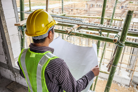 Asian business man construction engineer worker in protective helmet and blueprints paper on hand at house building siteの写真素材