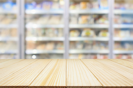wood table with supermarket commercial refrigerators freezer showing frozen foods abstract blur backgroundの写真素材
