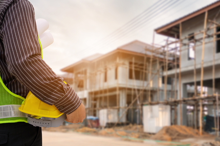 Asian business man construction engineer worker in protective helmet and blueprints paper on hand at house building siteの写真素材