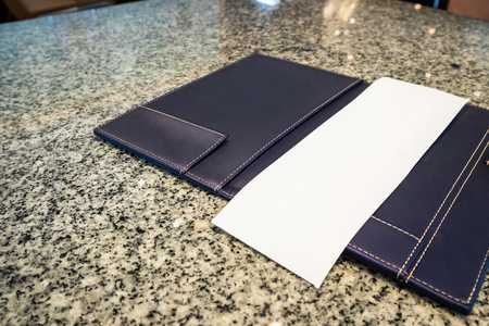 Blank empty white paper in restaurant payment billing receipt folder on granite tableの写真素材