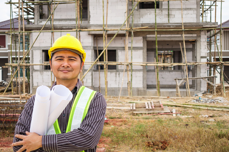 Asian business man construction engineer worker in protective helmet and blueprints paper on hand at house building siteの写真素材