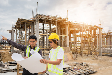 Asian business man construction manager and engineer worker in protective helmet hold blueprints paper on hand at house building siteの写真素材