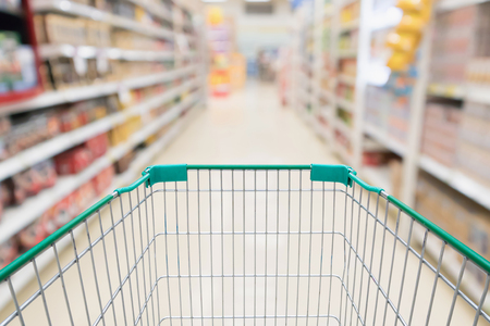 Empty shopping cart with abstract blur supermarket discount store aisle and product shelves interior defocused backgroundの写真素材